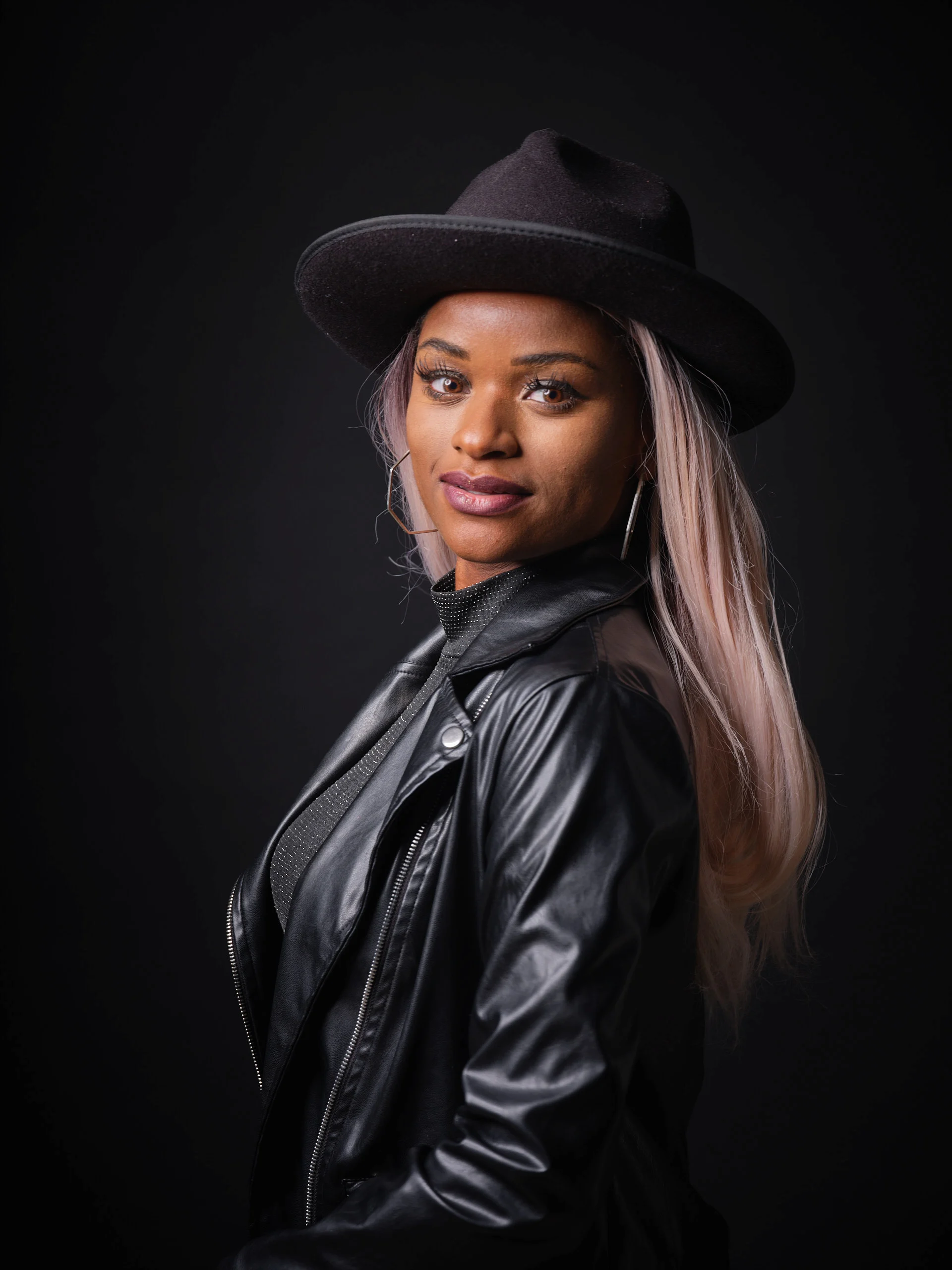 High-end studio portrait by San Francisco photographer; woman in a black fedora and leather jacket looking over her shoulder, captured on GFX medium format with a single Broncolor Para 133 for cinematic depth.