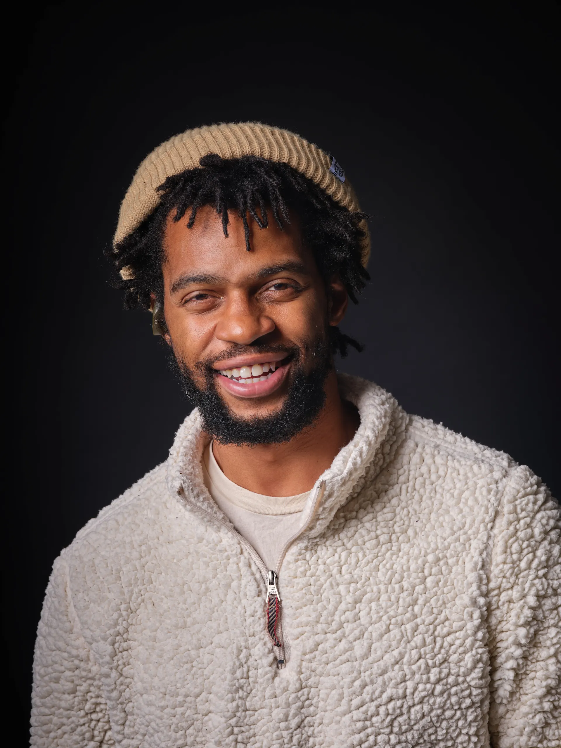 Close-up smiling studio portrait by San Francisco photographer; man in a white sherpa fleece and tan beanie, captured on GFX medium format with a single Broncolor Para 133 for soft, intentional fall-off.